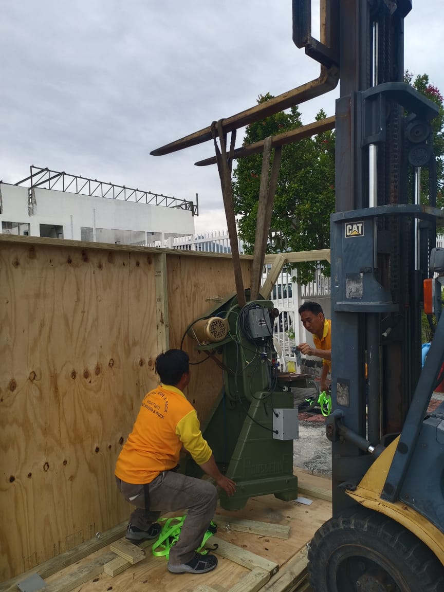 An M&C team using a CAT forklift to lower a green industrial machine into a wooden export crate